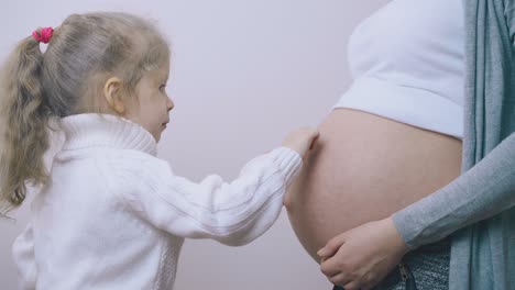 girl in sweater applies cream on pregnant mom belly in room