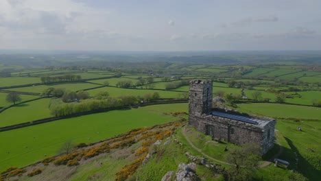 Aerial-view-of-a-remote-medieval-church,-overlooking-green-fields-in-the-uk