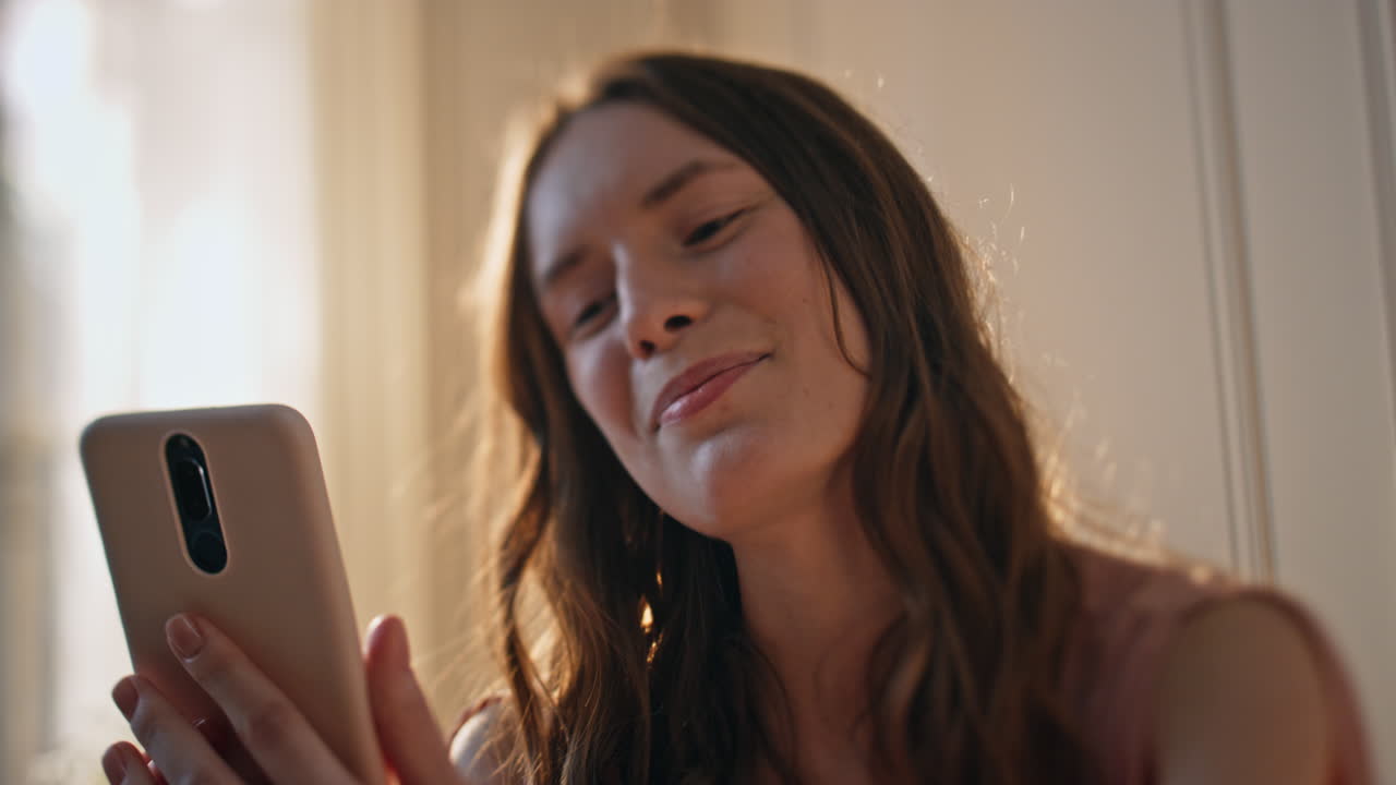 Closeup female waving mobile phone in sunny bedroom. Smiling girl videocalling