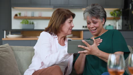 senior women laughing together at home, sharing moments on tablet