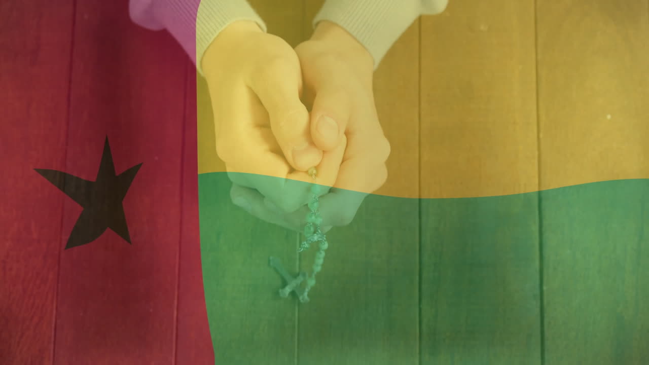 Holding rosary, hands over Guinea-Bissau flag background with animation elements