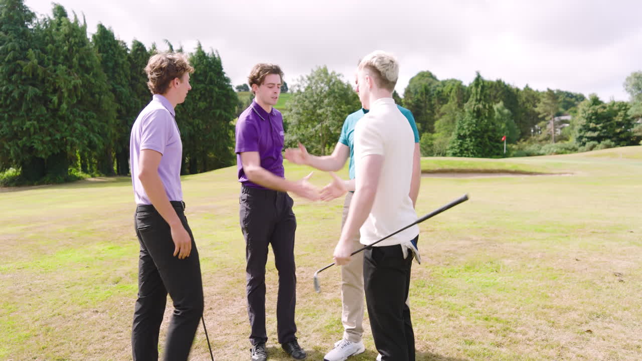 Male golf players wearing uniforms, holding clubs, talking and shaking hands on golf course
