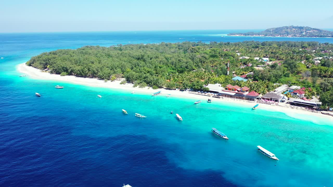 Beautiful tropical island with trees forest, white sandy beach surrounded by calm clear water of blue turquoise lagoon with boats floating, Bali