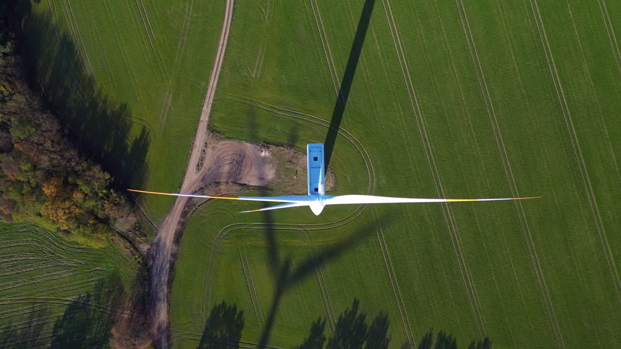 Wind turbine standing in green field next to highway autobahn in autumn Germany, generating renewable energy. Amazing aerial view flight drone camera pointing down