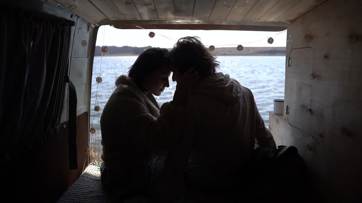 Un jeune couple amoureux, tête contre tête, à l'arrière d'une caravane au bord d'un lac.