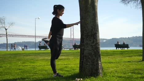 sportswoman leaning at tree and stretching leg