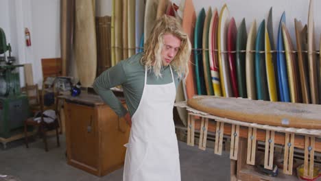 Caucasian-male-surfboard-maker-putting-on-a-protective-apron-in-his-studio