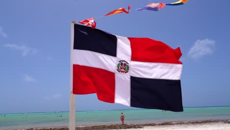 dominican republic flag waves in wind on a pristine caribbean beach