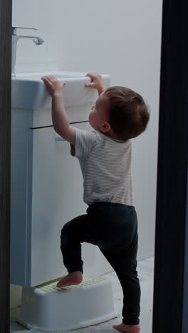 cute baby boy takes a stand out of the chest. smart kid stands on the prop to reach the tap. vertical video