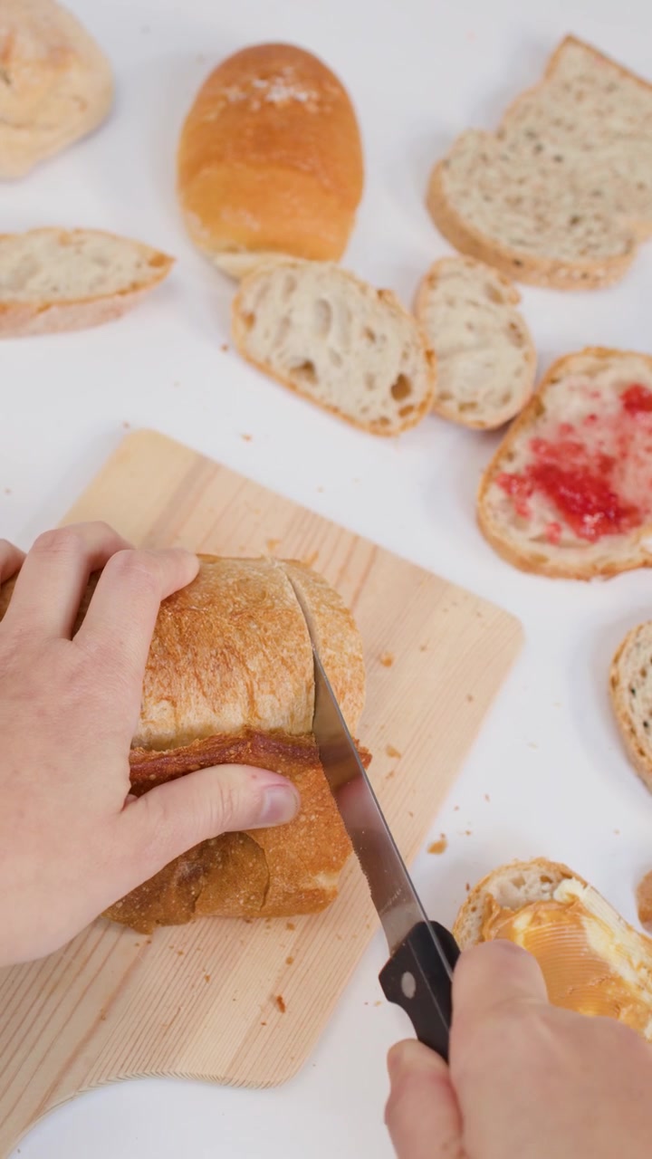Overhead shot of hands using a knife to slice crusty bread for breakfast preparation.