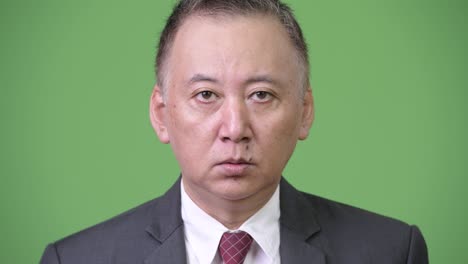 mature japanese businessman surprised against green background