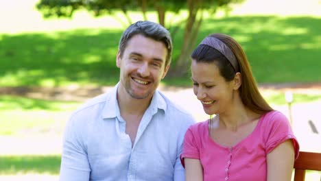 happy couple sitting on a park bench using tablet pc