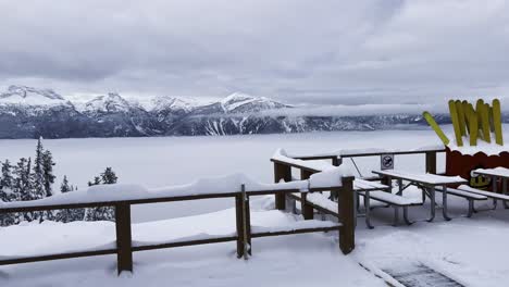 view panning over the mountain range south of the top of mt mackenzie revelstoke british columbia canada with a low cloud layer and snow covered railings with yellow skis in the background