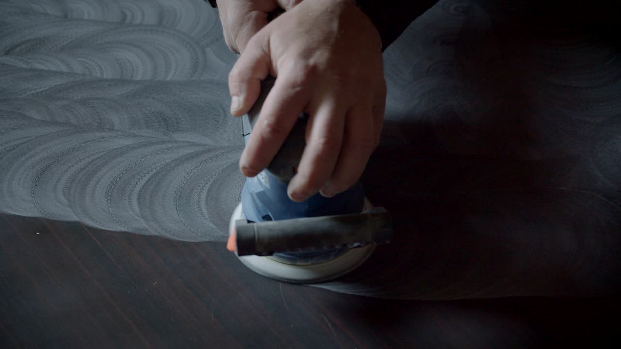 las manos masculinas usan la máquina de molienda para pulir la tabla de madera y hacer patrones circulares en ella en la fábrica de madera.