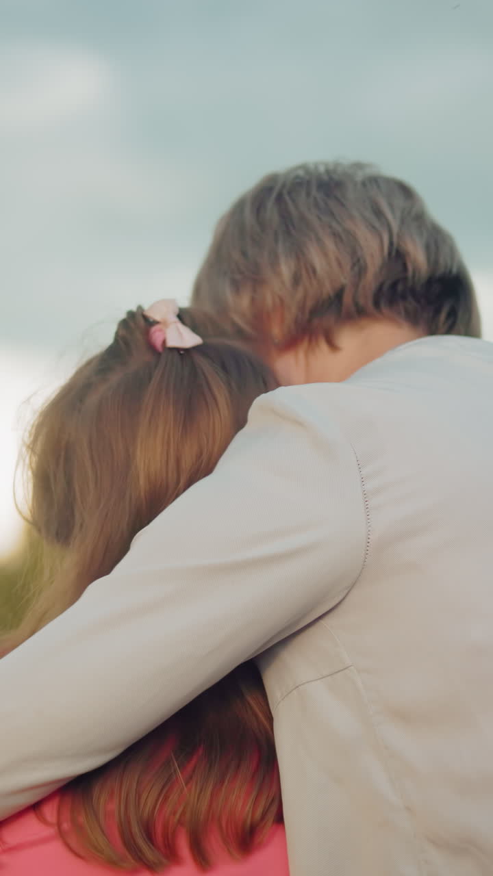 momento conmovedor como una madre abraza a su hija en rosa, ambos sentados en una bala de heno, compartiendo la cercanía en un campo expansivo bajo un cielo nublado