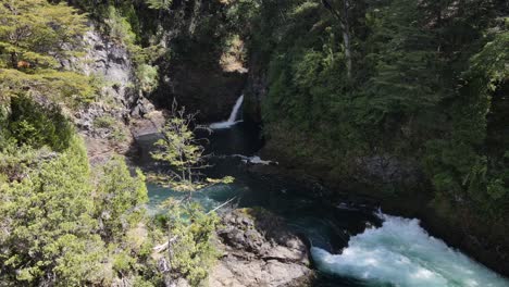 vuelo aéreo hacia adelante sobre un río que fluye mágico y una cascada rodeada de selva en la patagonia, argentina