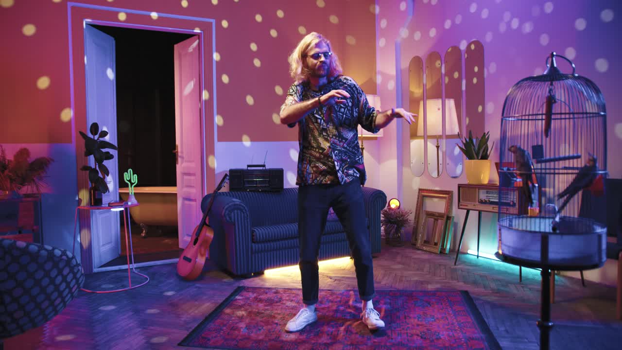 joven caucásico con estilo con el pelo largo en gafas bailando enérgicamente en una fiesta retro en casa