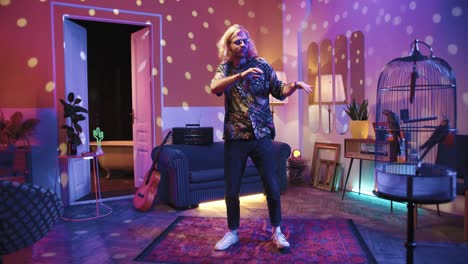 young stylish caucasian man with long hair in glasses dancing energetically in a retro party at home