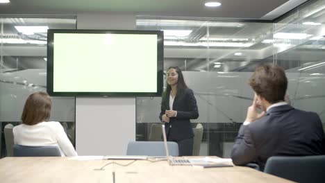 Smiling-speaker-talking-and-pointing-at-display