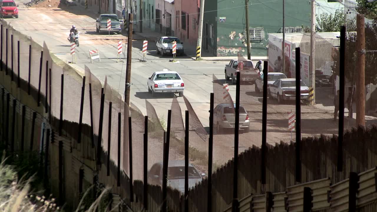 coches y una motocicleta conducen por una calle, un peatón cruza y otras personas se paran a un lado