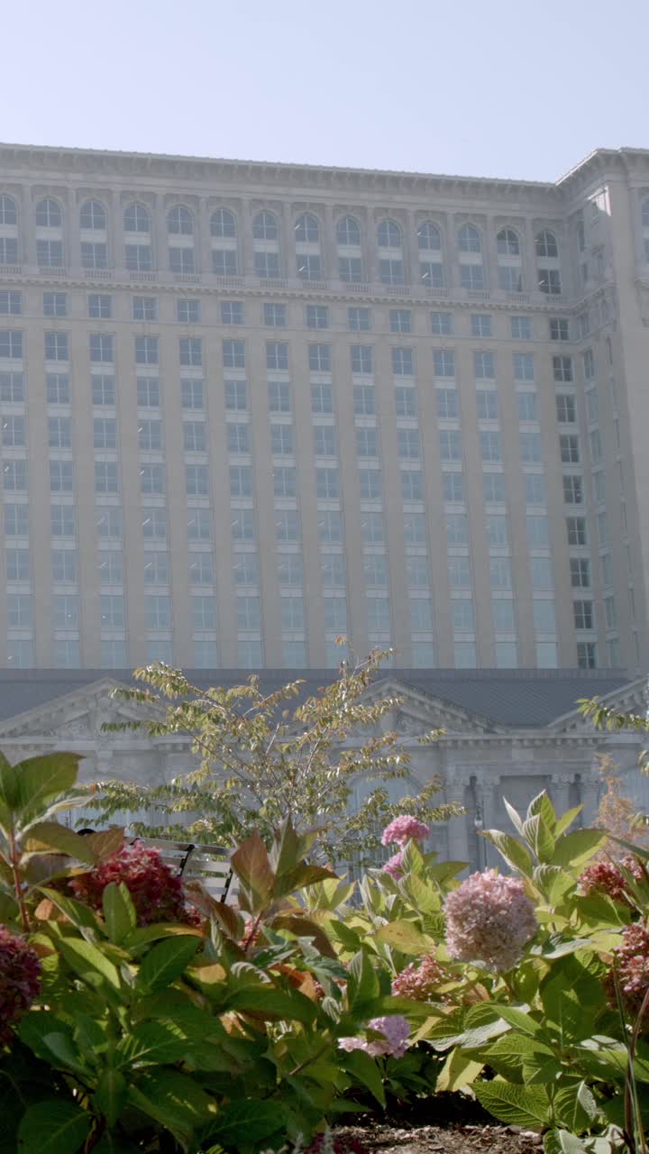 Vídeo vertical de la estación central de Míchigan en Detroit, Míchigan, con flores en primer plano. Escena de monumento urbano capturada en exteriores con luz natural, ideal para viajes y arquitectura.