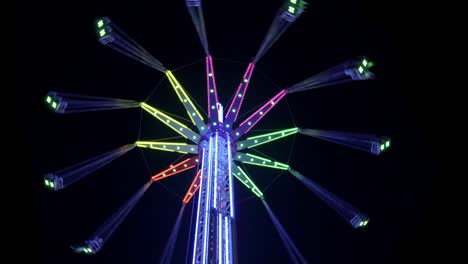 4k video of a swing tower ride, also known as vertical swing and flying tower covered with multicolored led lights spinning on the dark night black sky background.