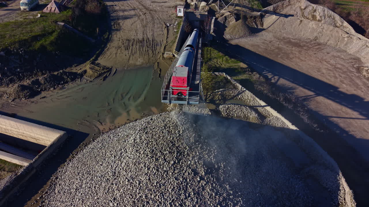 Construction site bustling with activity as gravel is meticulously processed and piled high against a clear blue sky