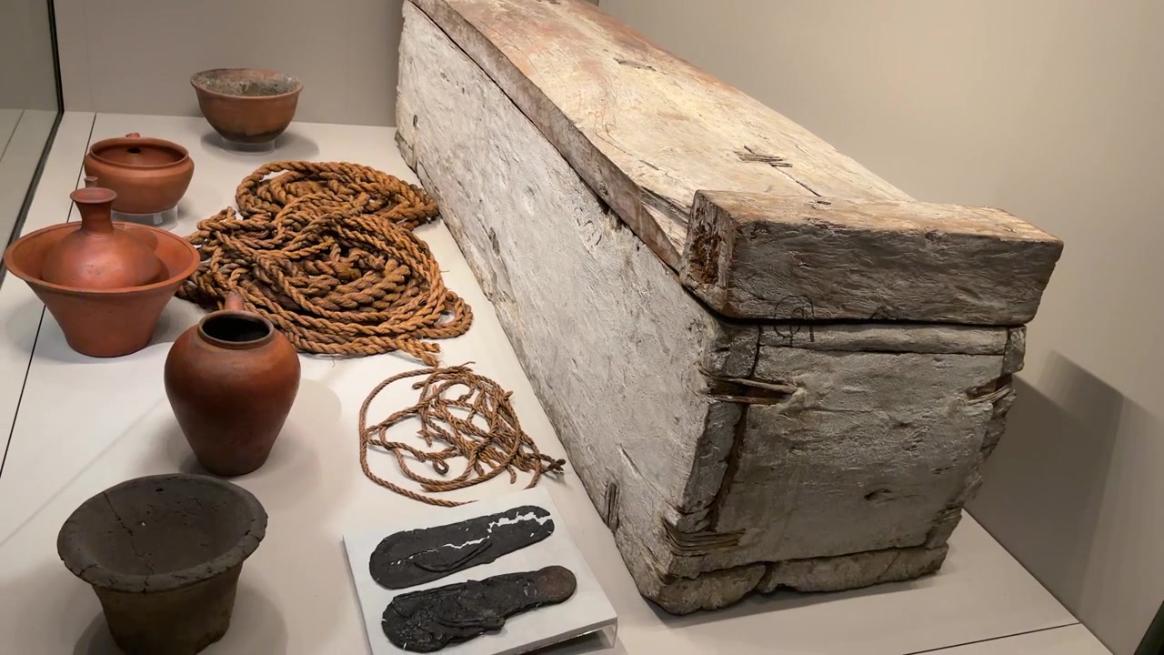 Inquadratura ampia statica di un sarcofago di legno invecchiato con vasi di argilla e corda di canapa.