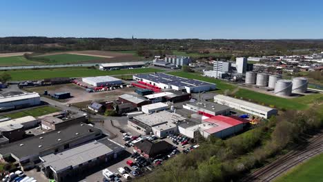 roofs of warehouses and factories in american suburb. parking cars, trucks and trailers. sunny day in spring. silo storage of company. blue sky with hills in distance. aerial wide shot.