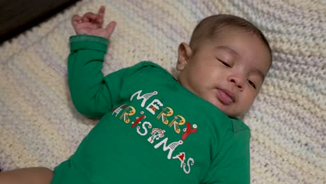 Adorable-Lindo-Bebé-Indio-Vestido-Con-Un-Traje-Verde-Festivo-De-Feliz-Navidad-Acostado-En-Una-Manta-Mientras-Se-Está-Cambiando