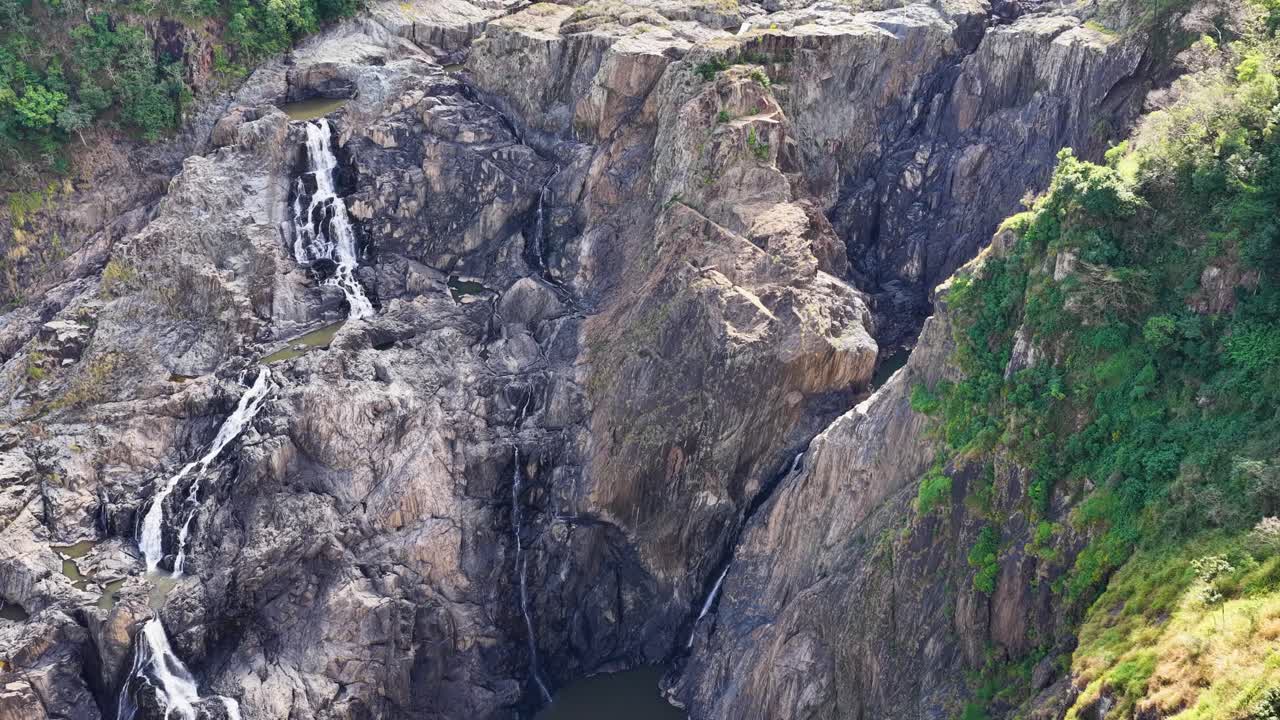 Aerial footage captures cascading waterfalls amidst rocky cliffs and lush greenery in Port Douglas, Australia