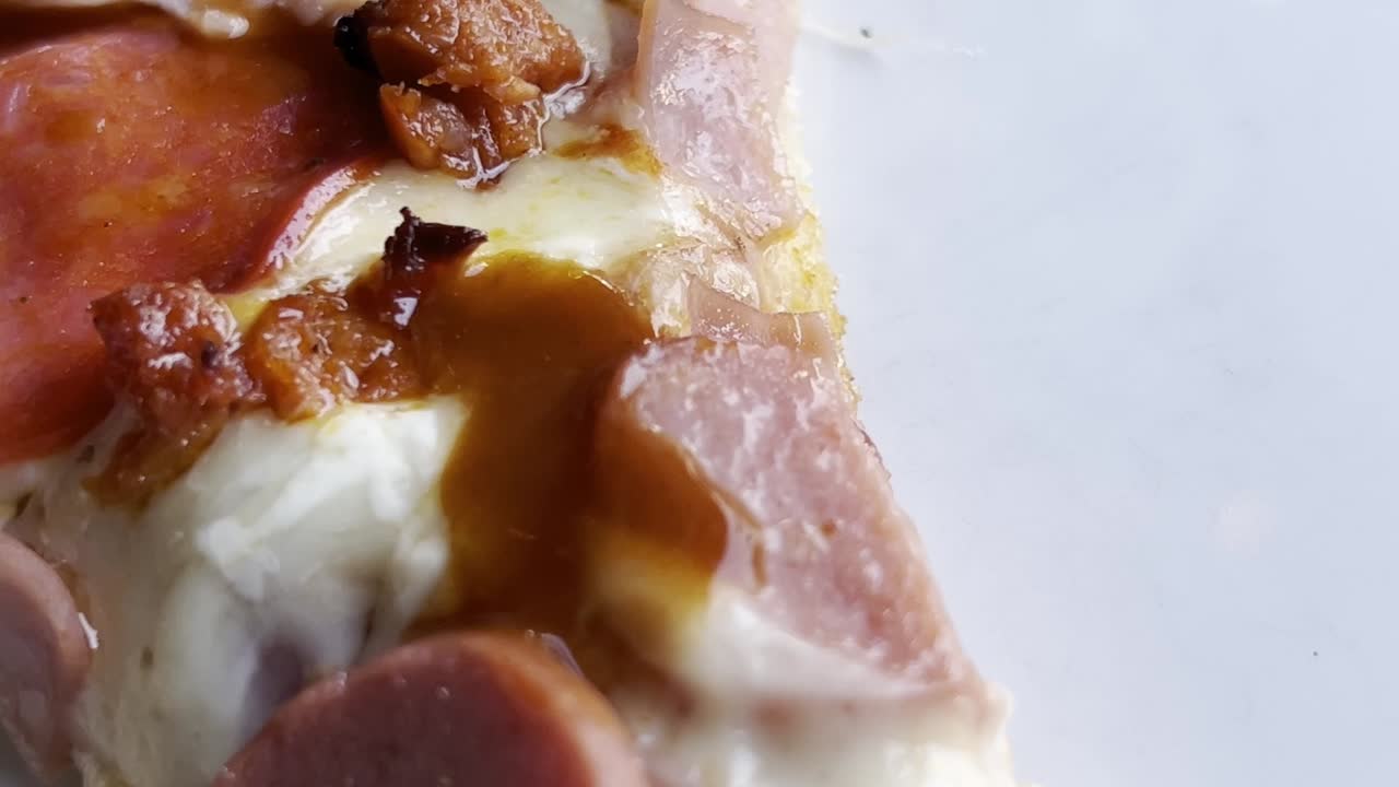 Pan left shot of pizza with pepperoni, ham, and melted cheese on a white background. Close-up food styling detailed shot