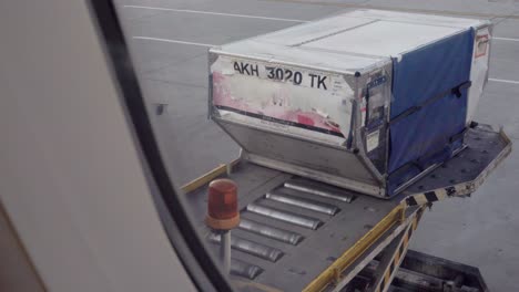 view from the window of a passenger plane of luggage pods being loaded