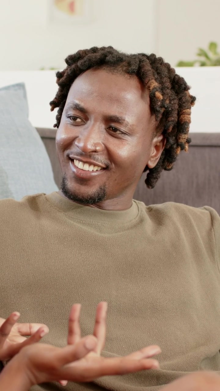 Video verticale: Uomo in maglione color oliva che reagisce a mani che gesticolano, sorridendo a una battuta a casa.