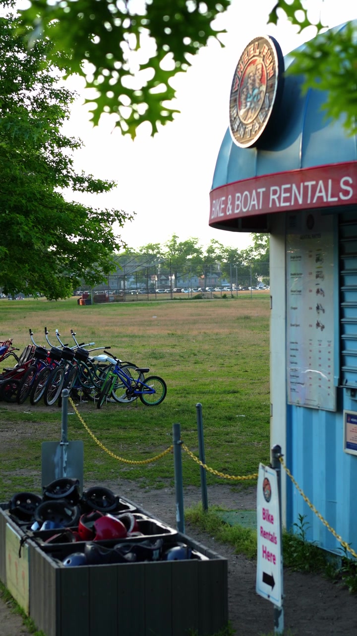 New York, USA, 5. juni 2026: Sykkelutleiekiosk ved siden av parkerte sykler i park. Vertikalt bilde viser hjelmer, skilt, gress og trær