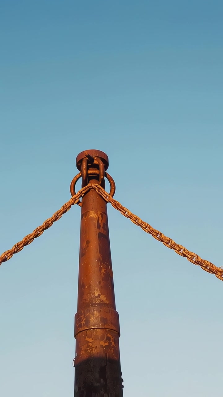 Video vertical: Cámara alejándose para revelar un poste al aire libre con cadenas y anillos, mostrando el cielo.