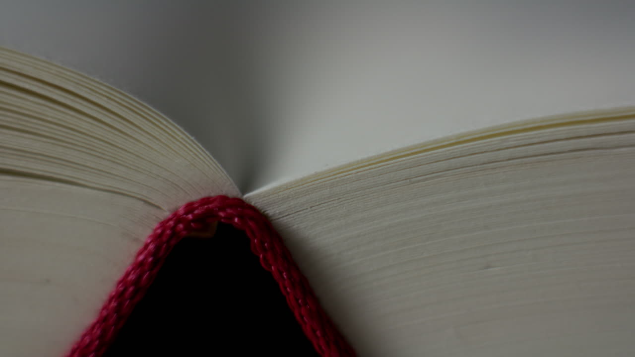 Primo piano del dorso di un libro aperto e delle pagine sovrapposte, ripreso con un movimento lento della camera da sinistra a destra. Dettaglio calmo e senza tempo che trasmette conoscenza, lettura e narrazione