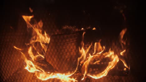 fire in a fireplace in slow motion with pieces of wood through a tiled grill