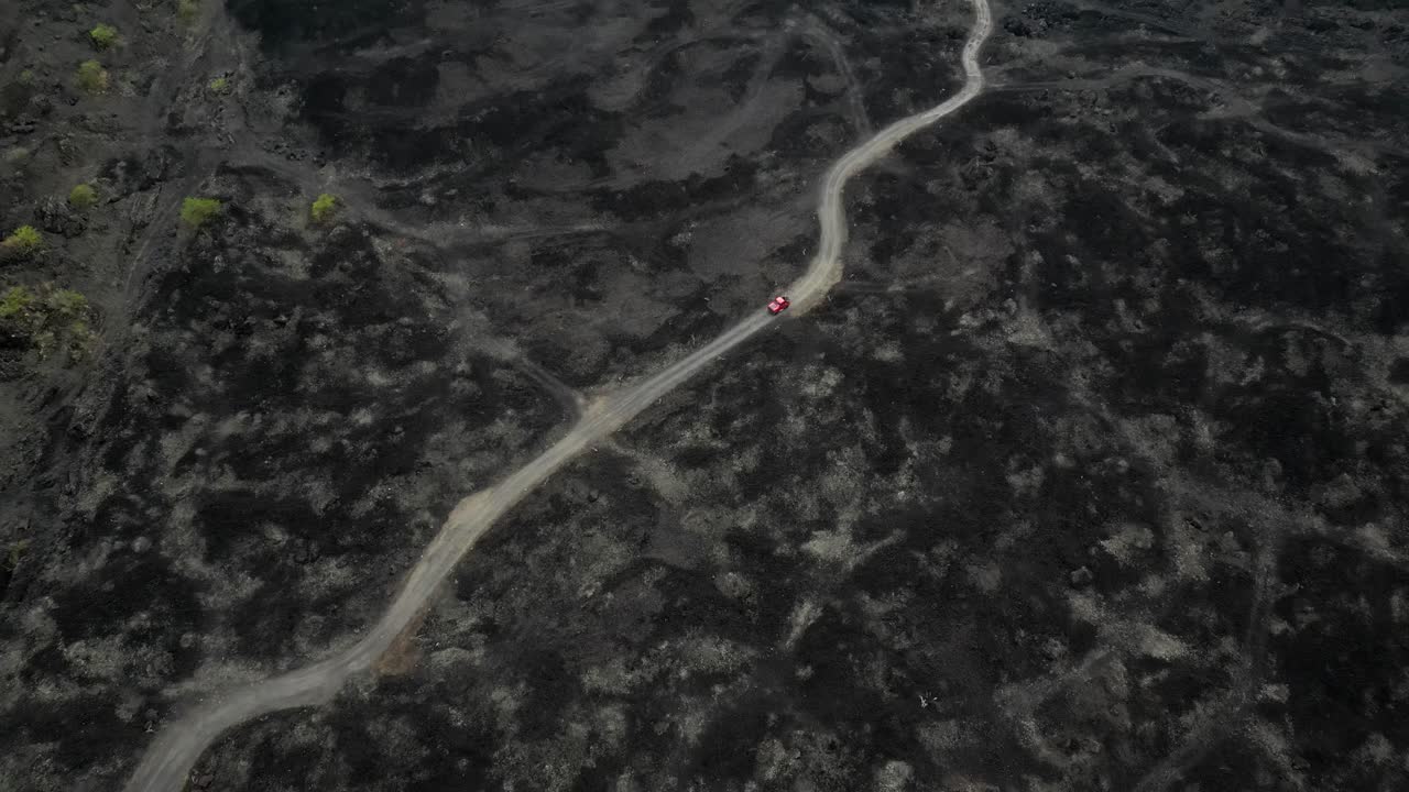 Red Jeep drives on new road built on volcanic lava at Mount Batur Bali
