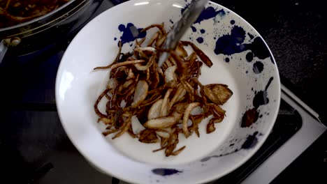 Golden Brown Crispy Fired Sliced Onions Being Placed On A Plate