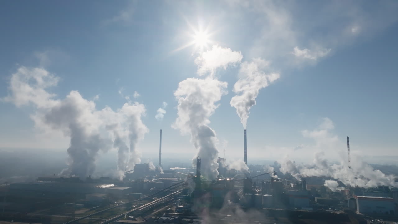 Panorama aereo con drone ad alta quota della zona industriale di Štětí con molteplici ciminiere, grandi vasche circolari e il vicino corridoio fluviale visibile ai margini dell'inquadratura