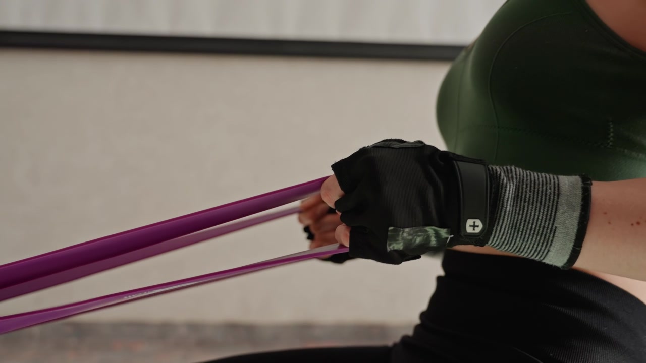 Closeup of feet and hands using resistance band on mat, gloves gripping handle, wrist and forearm tension visible, precise form, focus on technique and control, home training detail shots