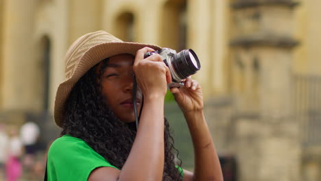 female tourist wearing straw sun hat with camera on vacation in oxford uk exploring city walking along broad street taking photos of the sheldonian theatre 1