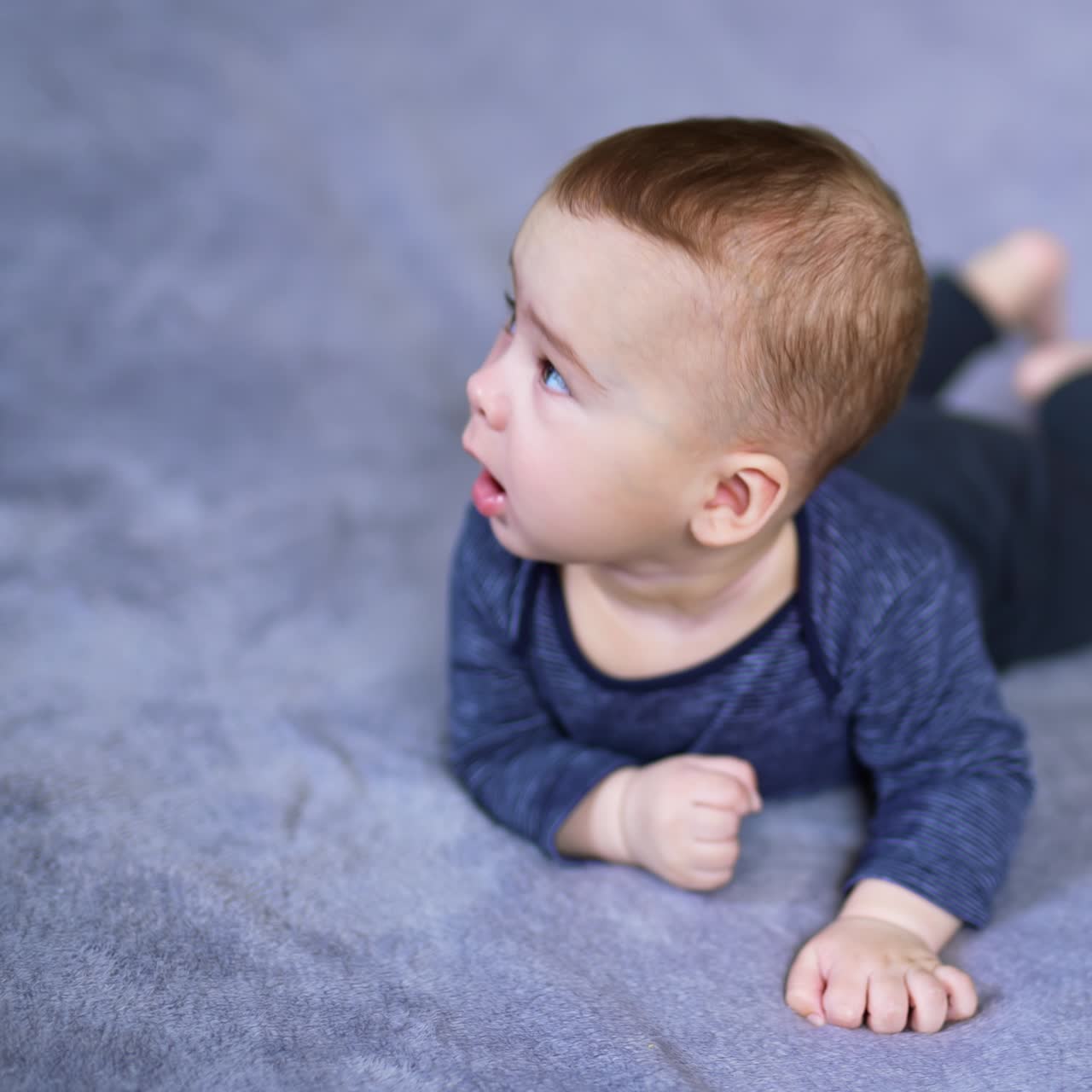 Cute healthy boy lies on a soft plaid. Little infant child turns around and looks up on the big bed. Blurred backdrop