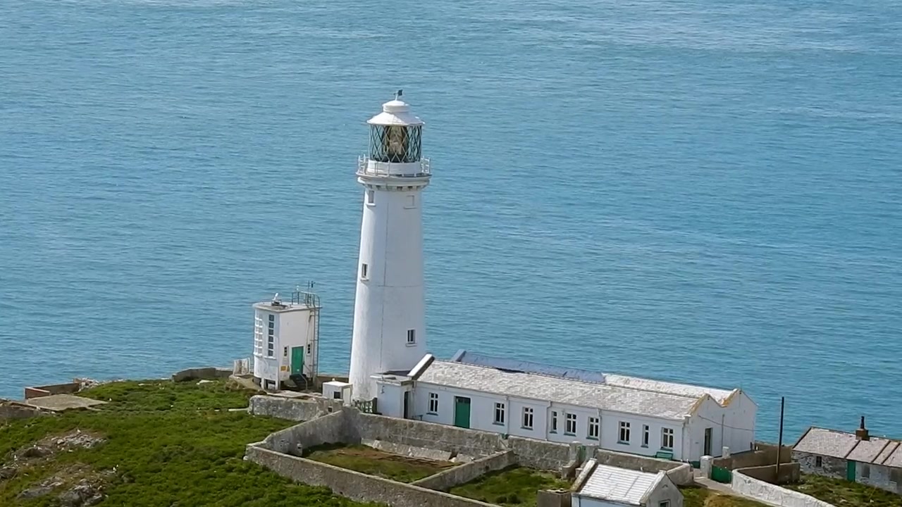 Solrigt South Stack ø-fyrtårn med rolig blå havbaggrund i Holyhead, Nordwales.