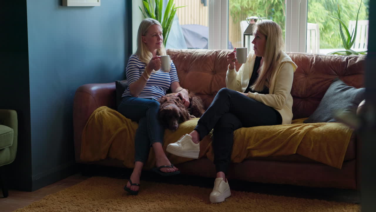 Two women chatting on a couch with their dog