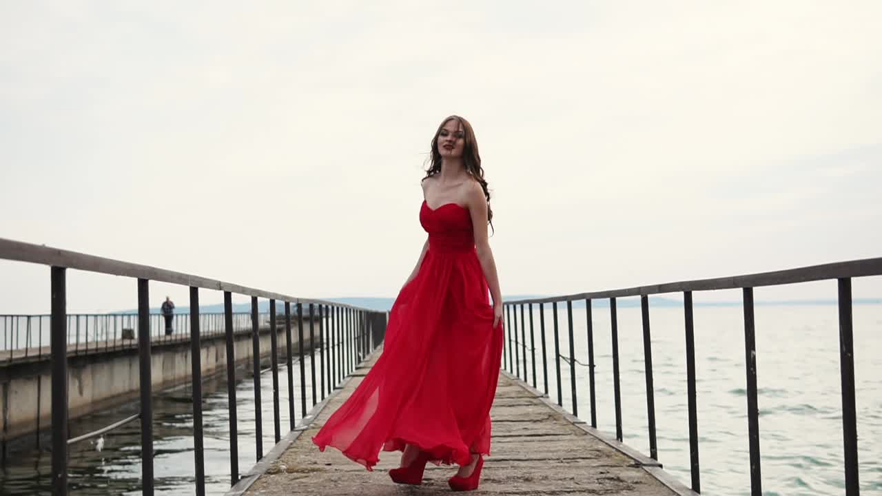 Mulher de Vestido Vermelho Caminhando em um Píer à Beira-Mar