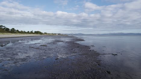 Vuelo-Lento-Durante-El-Día-Sobre-La-Playa-De-La-Bahía-De-Dundalk,-Justo-Por-Encima-De-La-Arena,-Con-Una-Dispersión-De-Pájaros