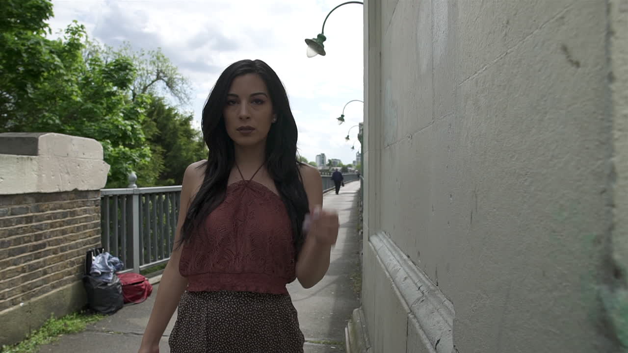 흰색 벽돌 벽의 왼쪽 팬에는 런던의 다리에서 포즈를 취하며 카메라를 향해 걸어가는 라틴계 히스패닉 모델이 나와 있습니다.