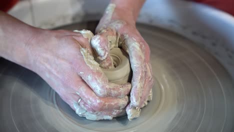 clay jar being sculpted on a potters wheel by female hands, close up view